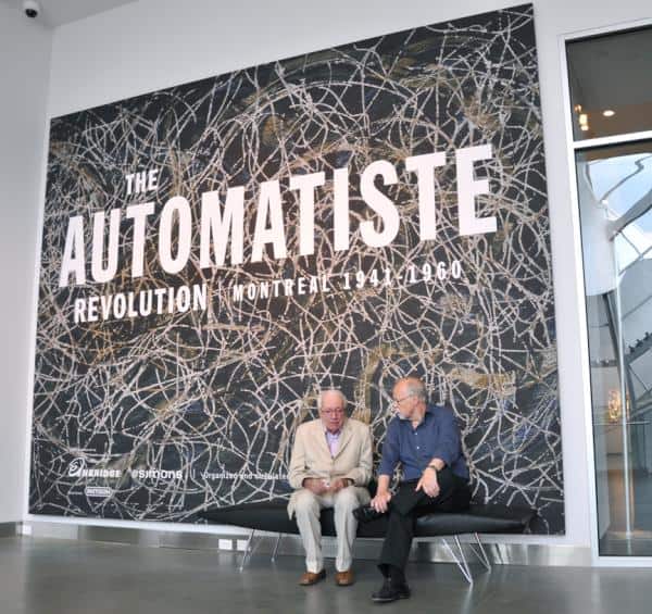 L'artist Marcel Barbeau et le commissaire Roald Nasgaard. Devant la banière de l'exposition The Automatiste Revolution ayant lieu à la Art Gallery of Alberta. Tableau reproduit sur la banière : Rosier-feuilles de Marcel Barbeau.